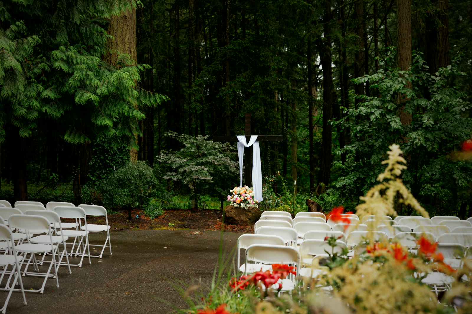 The ceremony site empty and waiting: rows of white chairs, a paved aisle, dense Douglas fir all around